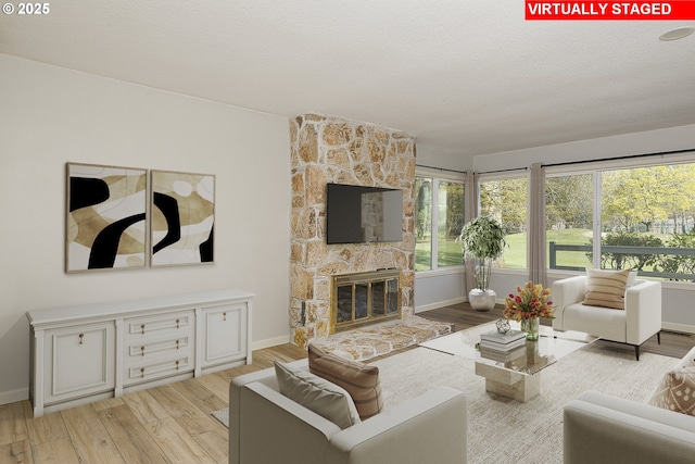 living room with light wood-type flooring, a healthy amount of sunlight, a fireplace, and a textured ceiling