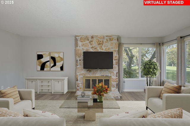 living area with a textured ceiling, wood finished floors, a stone fireplace, and a wealth of natural light