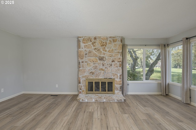 unfurnished living room with a stone fireplace, baseboards, wood finished floors, and a textured ceiling