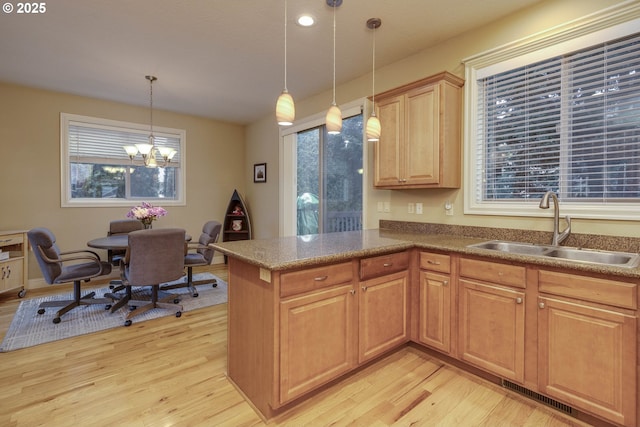 kitchen featuring visible vents, decorative light fixtures, light wood-type flooring, a peninsula, and a sink