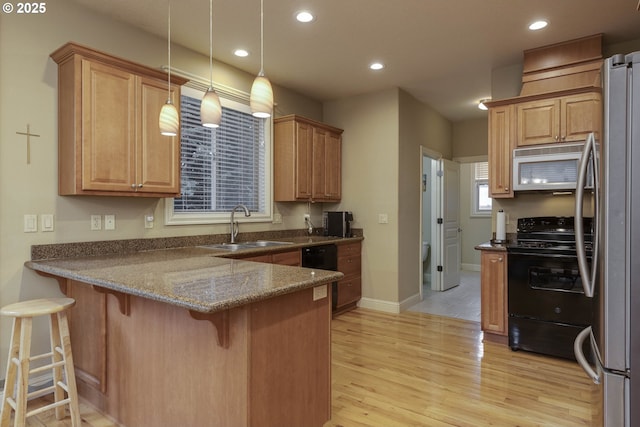 kitchen with white microwave, black range with electric stovetop, a peninsula, freestanding refrigerator, and a sink