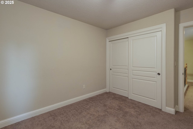 unfurnished bedroom featuring a closet, carpet flooring, a textured ceiling, and baseboards