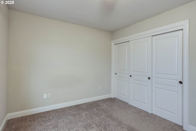 unfurnished bedroom with a closet, carpet flooring, a textured ceiling, and baseboards