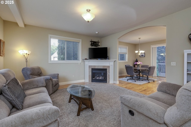 living room featuring wood finished floors, arched walkways, an inviting chandelier, a fireplace, and baseboards