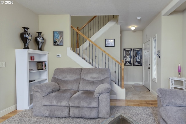 living room featuring baseboards, a textured ceiling, wood finished floors, and stairs