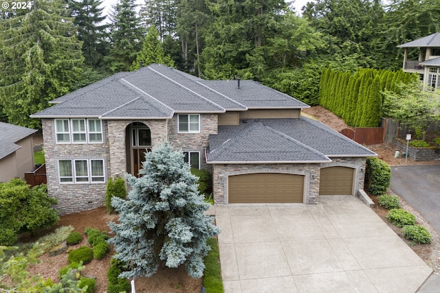 view of front of house featuring a garage, driveway, a shingled roof, stone siding, and fence