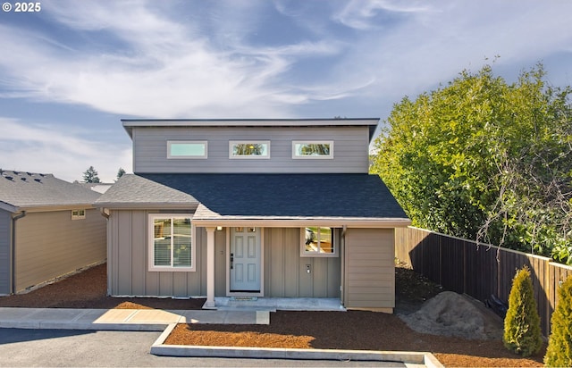 view of front of property with uncovered parking, a shingled roof, board and batten siding, and fence