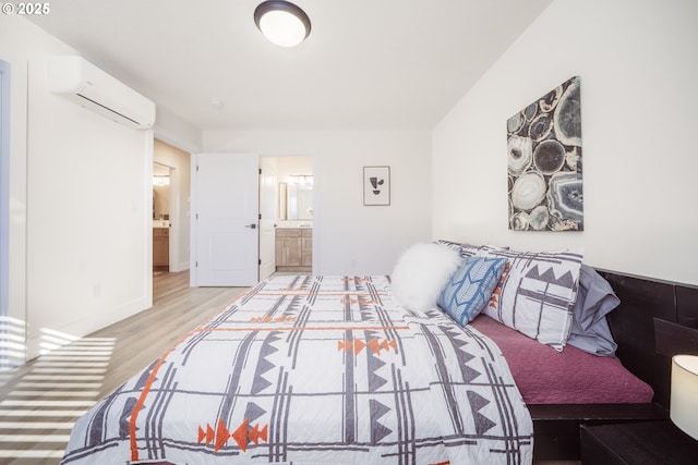 bedroom featuring a wall mounted air conditioner, ensuite bath, and light wood-style flooring