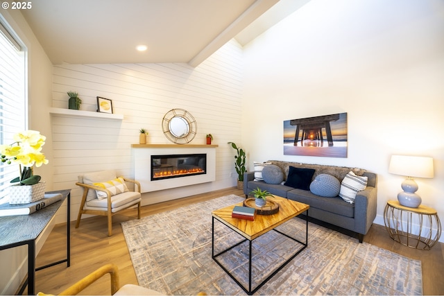 living area featuring high vaulted ceiling, a glass covered fireplace, and wood finished floors