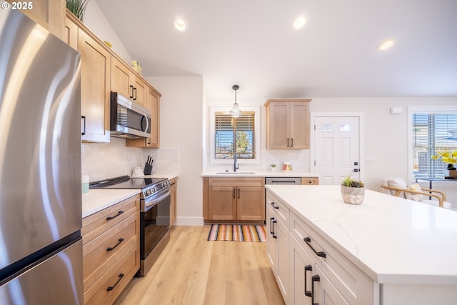 kitchen featuring light brown cabinets, stainless steel appliances, a sink, light wood-style floors, and decorative light fixtures