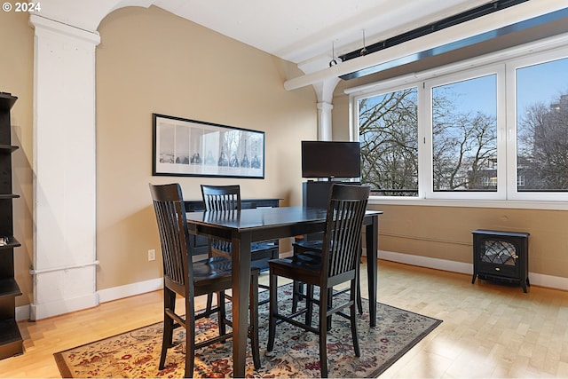 dining area featuring light wood-style floors, baseboards, a wood stove, and ornate columns