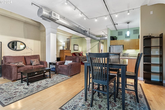 dining space with rail lighting, light hardwood / wood-style floors, and decorative columns