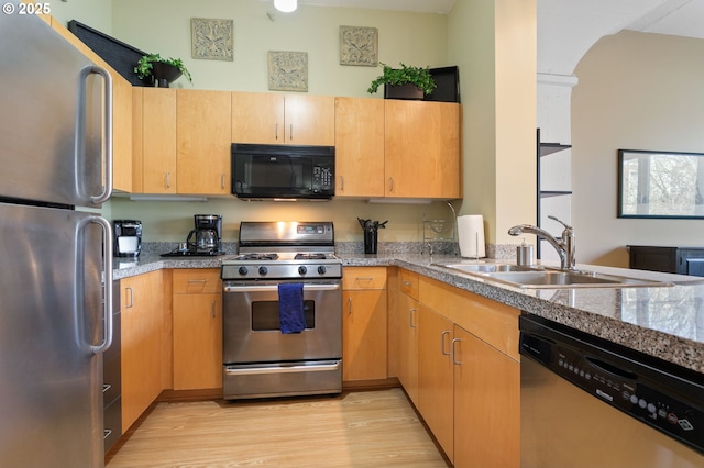 kitchen with appliances with stainless steel finishes, sink, light stone countertops, light brown cabinets, and light wood-type flooring