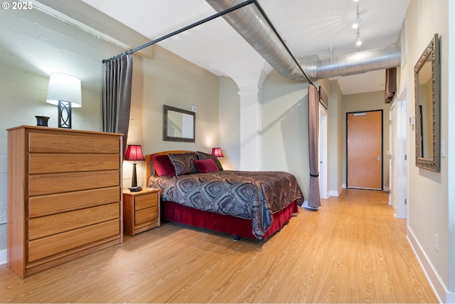 bedroom with light wood-style floors, rail lighting, baseboards, and ornate columns
