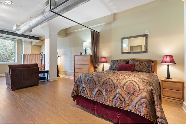 bedroom with baseboards, decorative columns, and wood finished floors