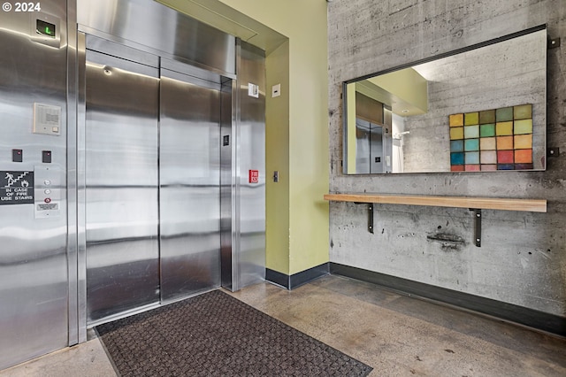 interior space with concrete flooring, elevator, and baseboards
