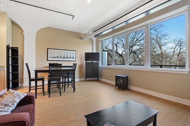 living room with track lighting, decorative columns, baseboards, light wood-style floors, and arched walkways