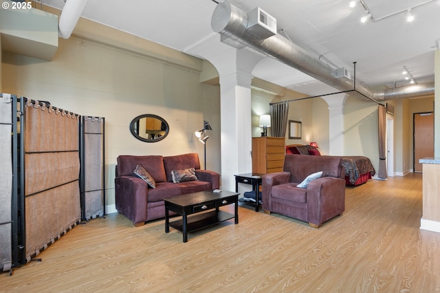 living area with ornate columns, arched walkways, track lighting, and light wood-type flooring