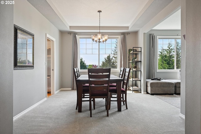 dining space featuring a chandelier, light carpet, a raised ceiling, and plenty of natural light