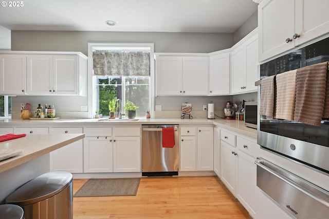 kitchen with appliances with stainless steel finishes, a warming drawer, a sink, light countertops, and light wood-style floors