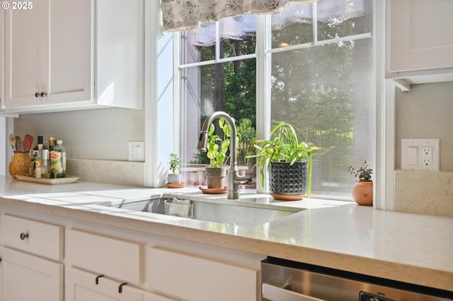 kitchen featuring stainless steel dishwasher, a sink, white cabinets, and light countertops