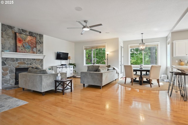 living room featuring light wood finished floors, ceiling fan, and a stone fireplace