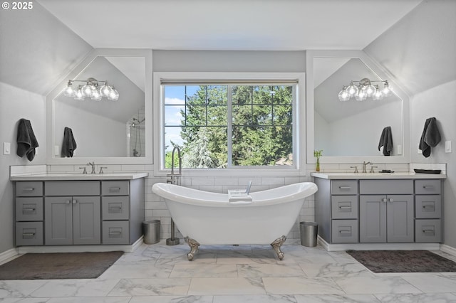 full bathroom featuring marble finish floors, a stall shower, a freestanding bath, and two vanities