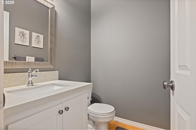 bathroom with toilet, vanity, baseboards, and wood finished floors