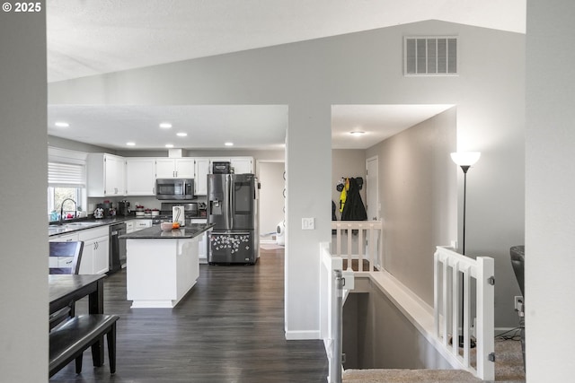 kitchen with vaulted ceiling, appliances with stainless steel finishes, white cabinetry, a center island, and dark wood-type flooring