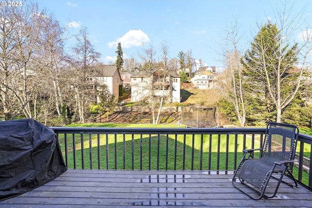 wooden deck featuring a trampoline, grilling area, and a lawn