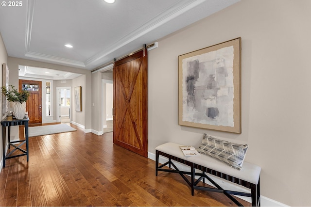 foyer entrance featuring a barn door, baseboards, a raised ceiling, wood-type flooring, and ornamental molding