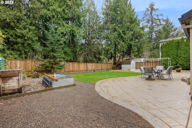 view of yard with a shed, a vegetable garden, a fenced backyard, an outbuilding, and a patio area