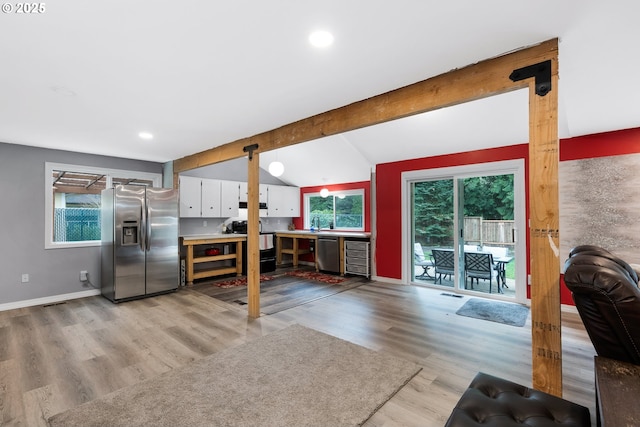 kitchen featuring baseboards, lofted ceiling with beams, white cabinets, light wood-style floors, and appliances with stainless steel finishes