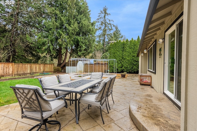view of patio / terrace featuring a fenced backyard, outdoor dining space, and a storage shed