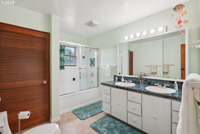 bathroom featuring double vanity, toilet, enclosed tub / shower combo, and a sink