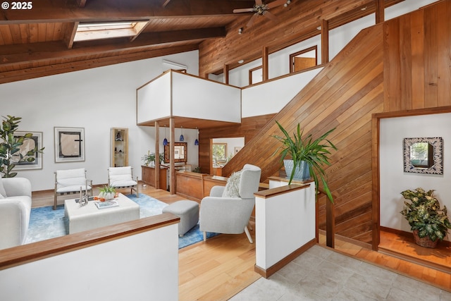 living room featuring wooden walls, beam ceiling, high vaulted ceiling, wooden ceiling, and a skylight