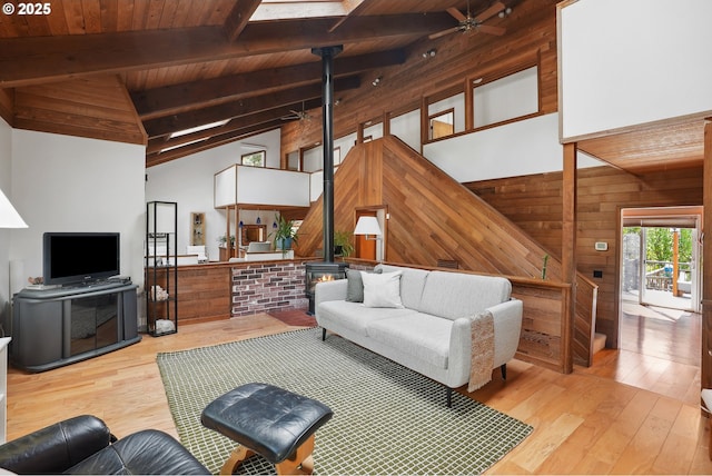 living room featuring wood-type flooring, a ceiling fan, a wood stove, and wood walls