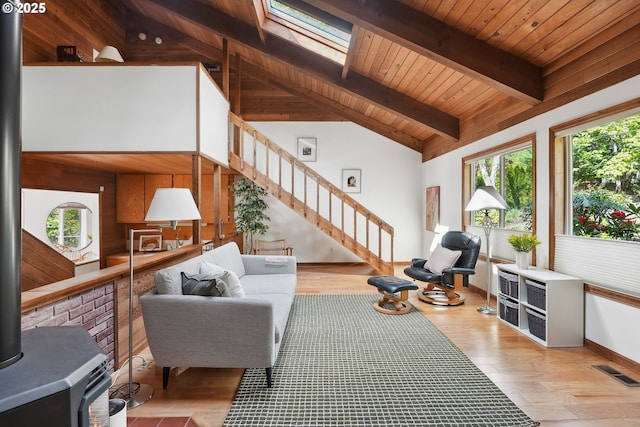 living area featuring vaulted ceiling with skylight, visible vents, a wood stove, wood finished floors, and stairs