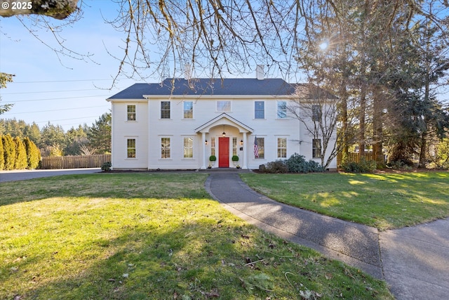 colonial home featuring a front yard, fence, and a chimney