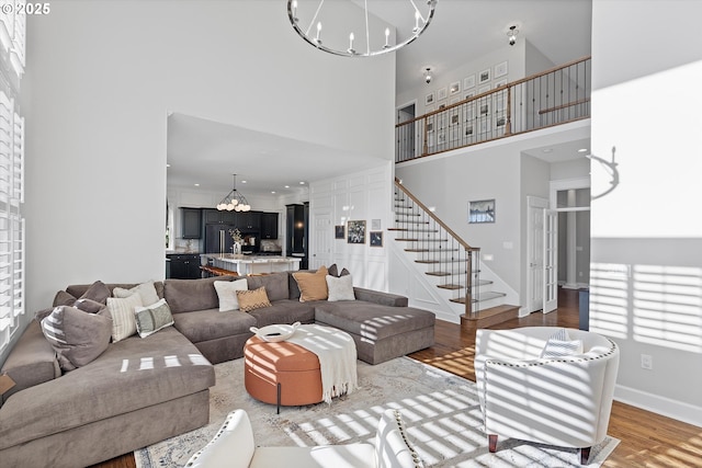 living area with a notable chandelier, wood finished floors, a towering ceiling, baseboards, and stairway