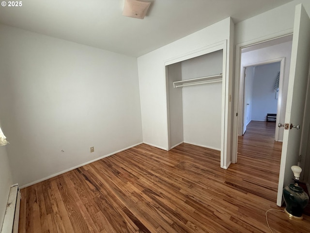 unfurnished bedroom with a baseboard heating unit, a closet, and wood-type flooring