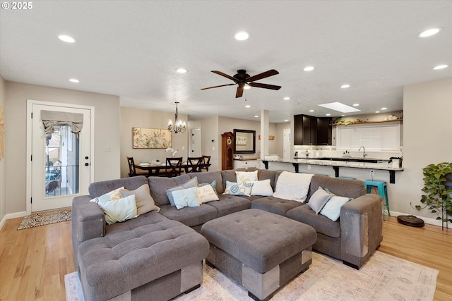 living room with sink, ceiling fan with notable chandelier, and light hardwood / wood-style flooring