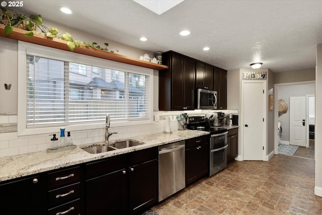 kitchen featuring stainless steel appliances, sink, light stone counters, and decorative backsplash