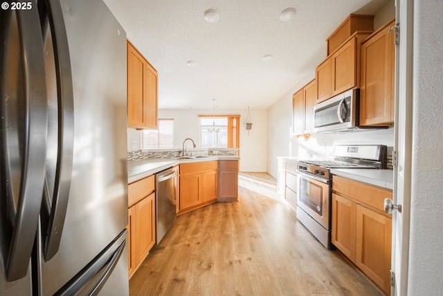 kitchen featuring pendant lighting, stainless steel appliances, sink, and light hardwood / wood-style floors