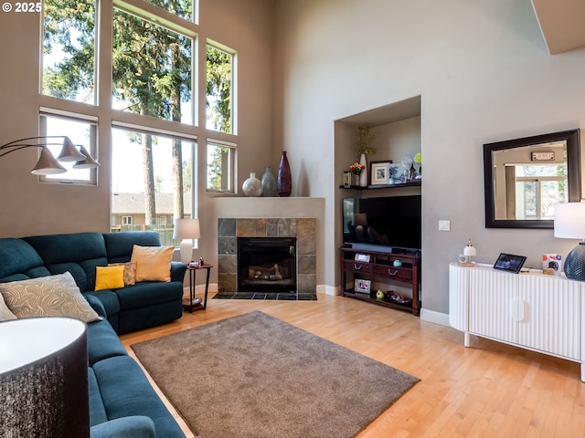 living area with a tiled fireplace, a high ceiling, baseboards, and wood finished floors