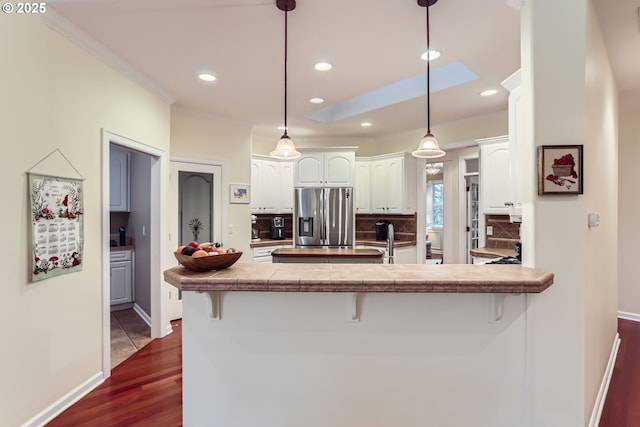 kitchen featuring stainless steel refrigerator with ice dispenser, white cabinets, a kitchen bar, decorative light fixtures, and kitchen peninsula