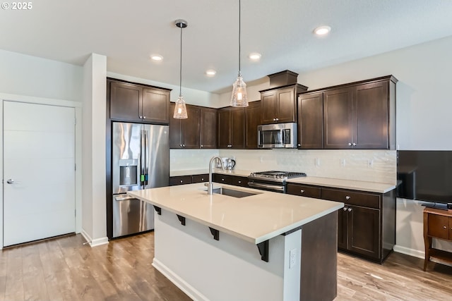 kitchen featuring sink, hanging light fixtures, stainless steel appliances, dark brown cabinetry, and decorative backsplash