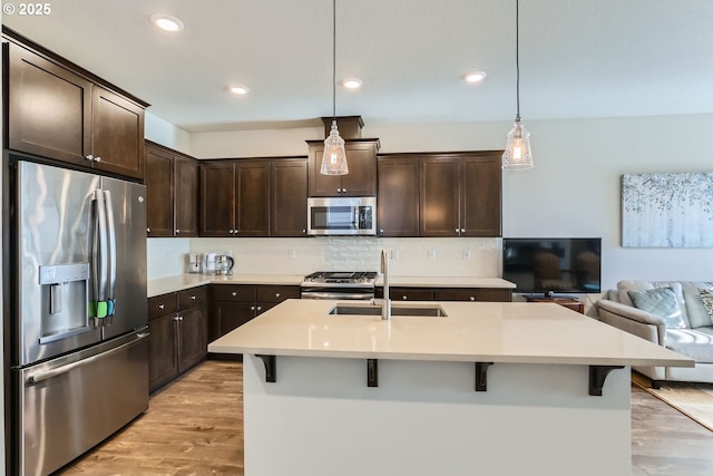 kitchen with appliances with stainless steel finishes, decorative light fixtures, sink, a kitchen bar, and dark brown cabinetry