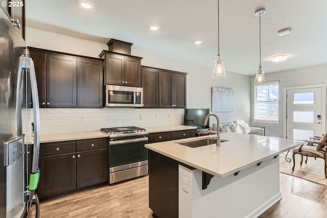 kitchen featuring decorative light fixtures, sink, light hardwood / wood-style floors, stainless steel appliances, and dark brown cabinets