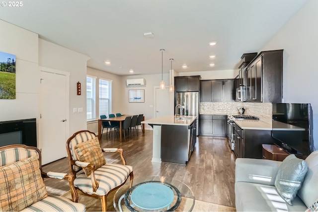 kitchen featuring a wall mounted air conditioner, a kitchen island with sink, pendant lighting, stainless steel appliances, and light hardwood / wood-style floors